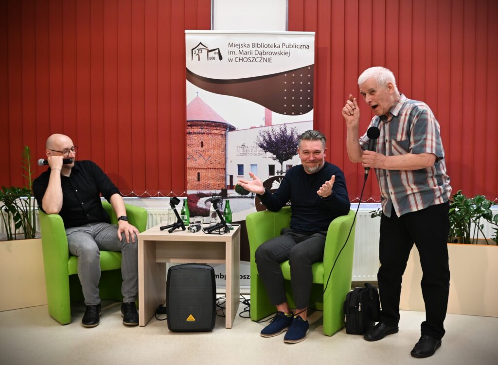 Od lewej siedzą: Marek Stelar i Przemysław Kowalewski, po prawej stoi starszy mężczyzna z mikrofonem w dłoni.