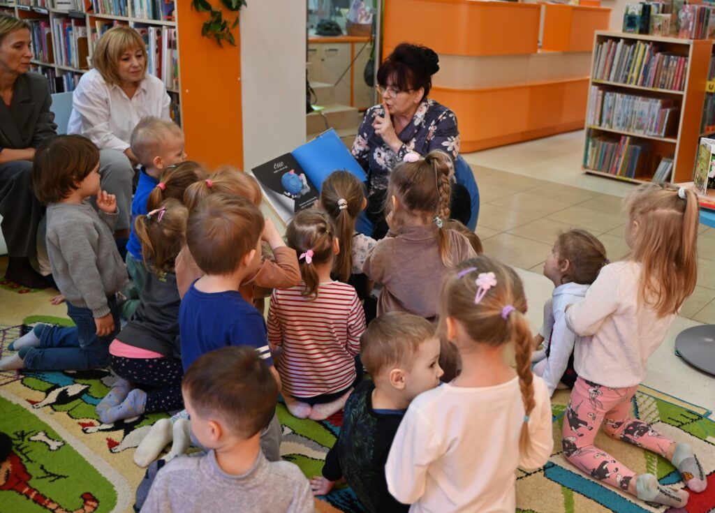 Bibliotekarka Irena Kozłowska czyta przedszkolakom książkę. Przykłada palec do ust.