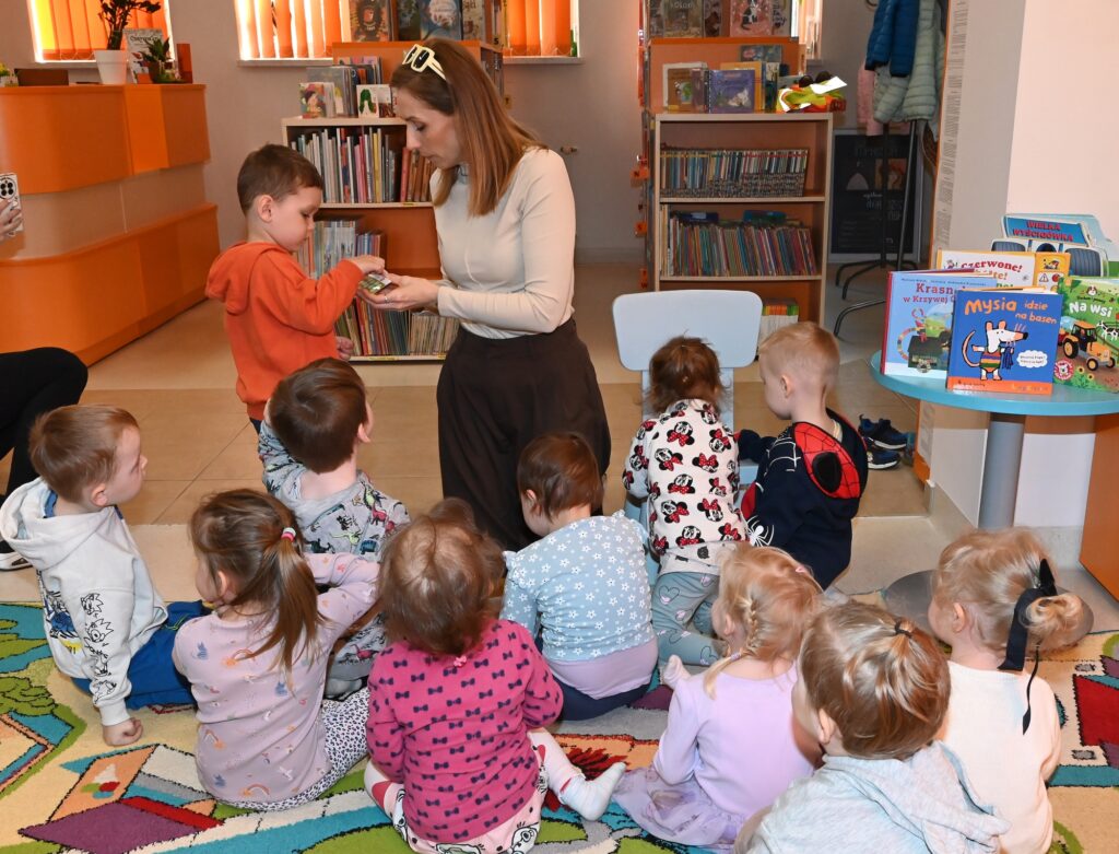 Bibliotekarka Izabela Szczyż pokazuje chłopcu kartę. Przed nimi siedzą dzieci.