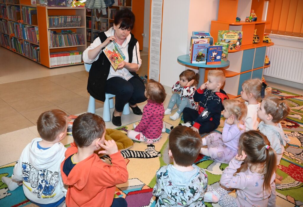 Bibliotekarka Irena Kozłowska pokazuje dzieciom książkę.
