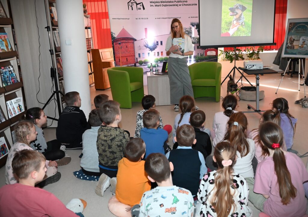 Marta Maj stoi przed dziećmi. W rękach trzyma książkę