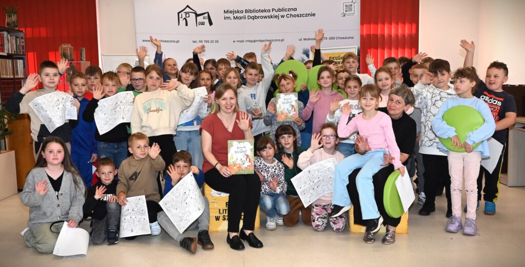 Zdjęcie grupowe. Wśród dzieci na pufach siedzą Magdalena Kiełbowicz i Małgorzata Narożna z dziewczynką na kolanach. Część osób trzyma książki lub rysunki.