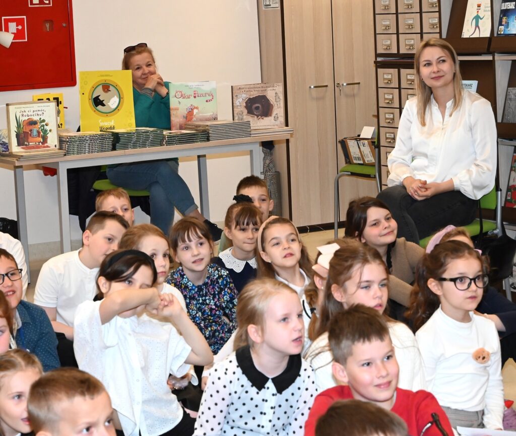 Dzieci. Z tyłu przy stole z książkami siedzi księgarka Maria Mińska.