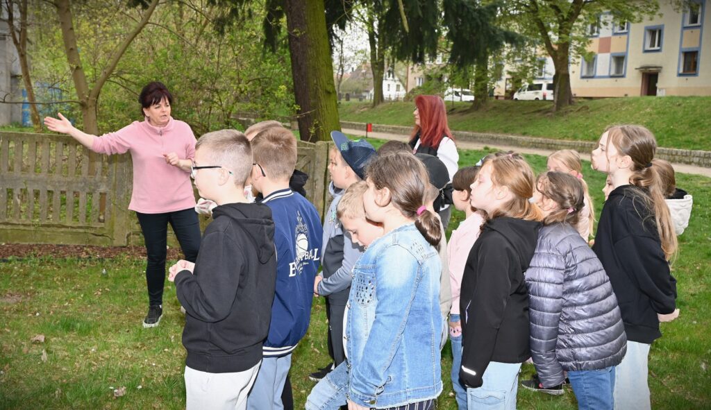 Bibliotekarka Irena Kozłowska razem z dziećmi stoją na trawie obok biblioteki.
