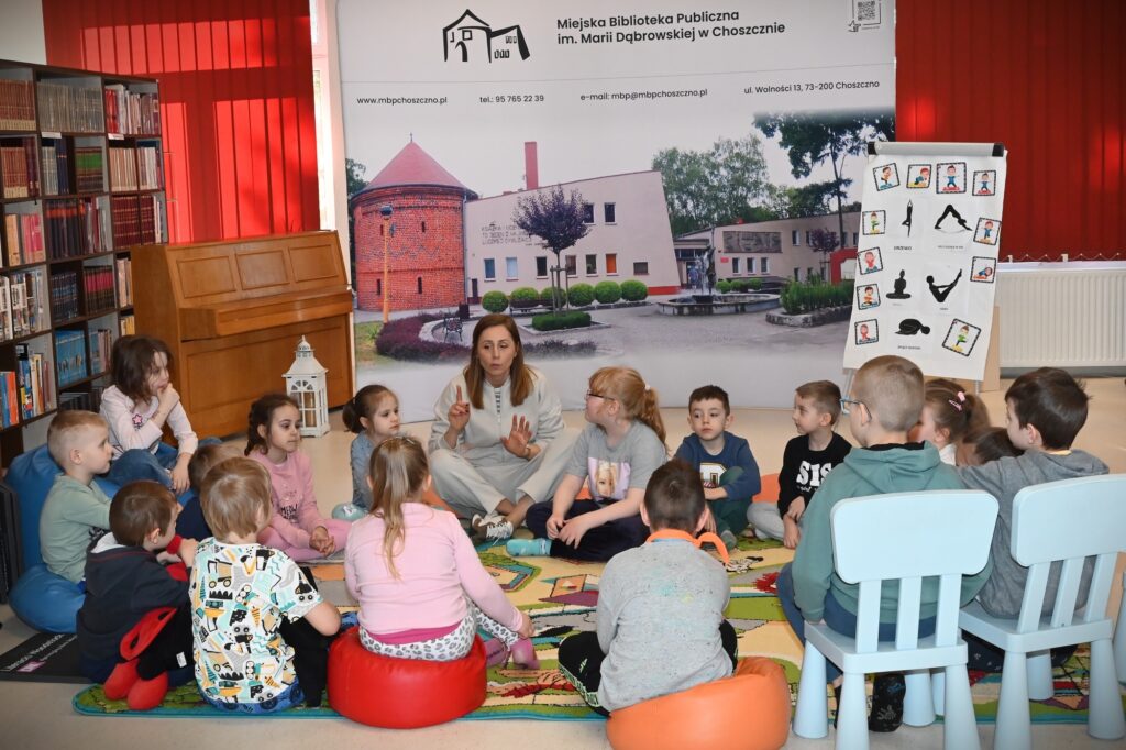 Dzieci siedzą w kręgu z bibliotekarką Izą Szczyż.