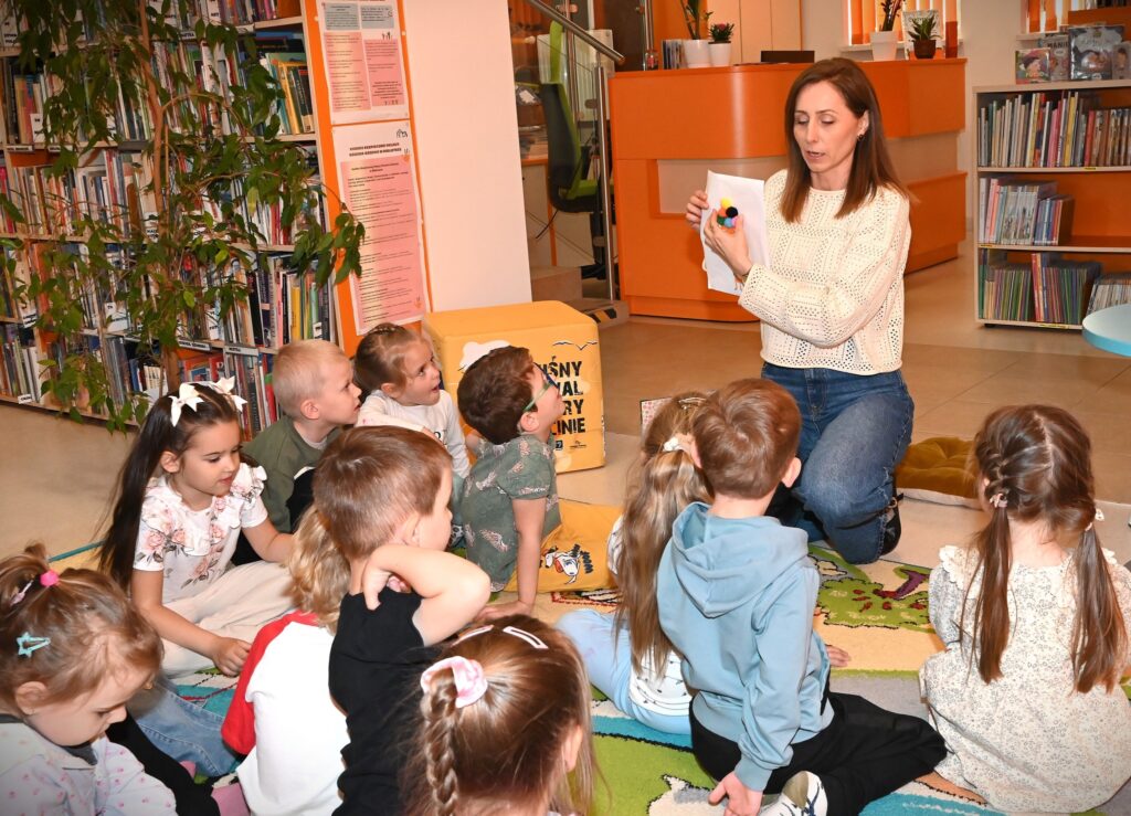 Bibliotekarka Iza Szczyz pokazuje dzieciom rysunek z przyklejonymi małymi pomponikami.