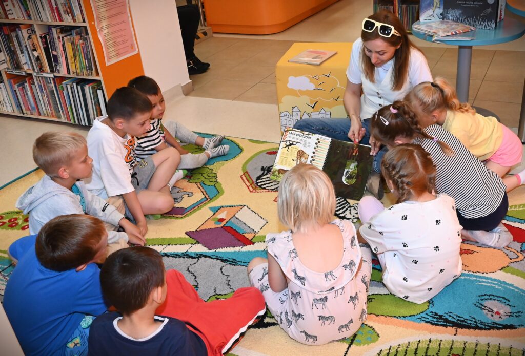 Bibliotekarka Izabela Szczyż pokazuje dzieciom książkę o lasach deszczowych.