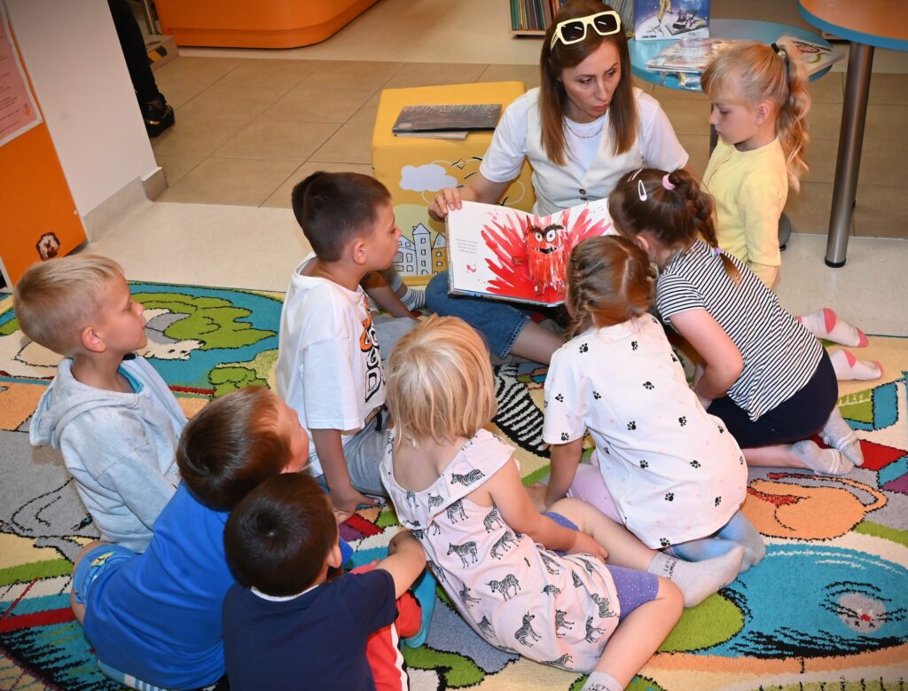 Bibliotekarka Izabela Szczyż pokazuje dzieciom książkę o emocjach.