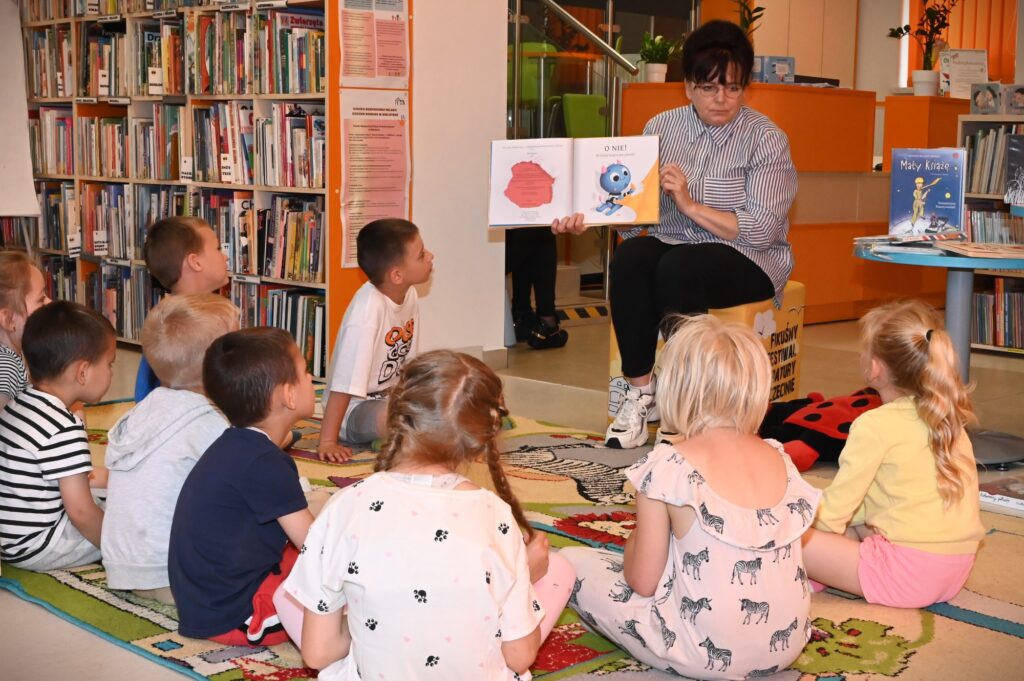 Bibliotekarka Irena Kozłowska pokazuje dzieciom otwartą książkę ,