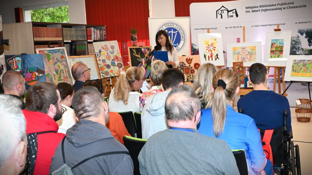 Katarzyna Jezierska stoi przed publicznością. Za nią obrazy.