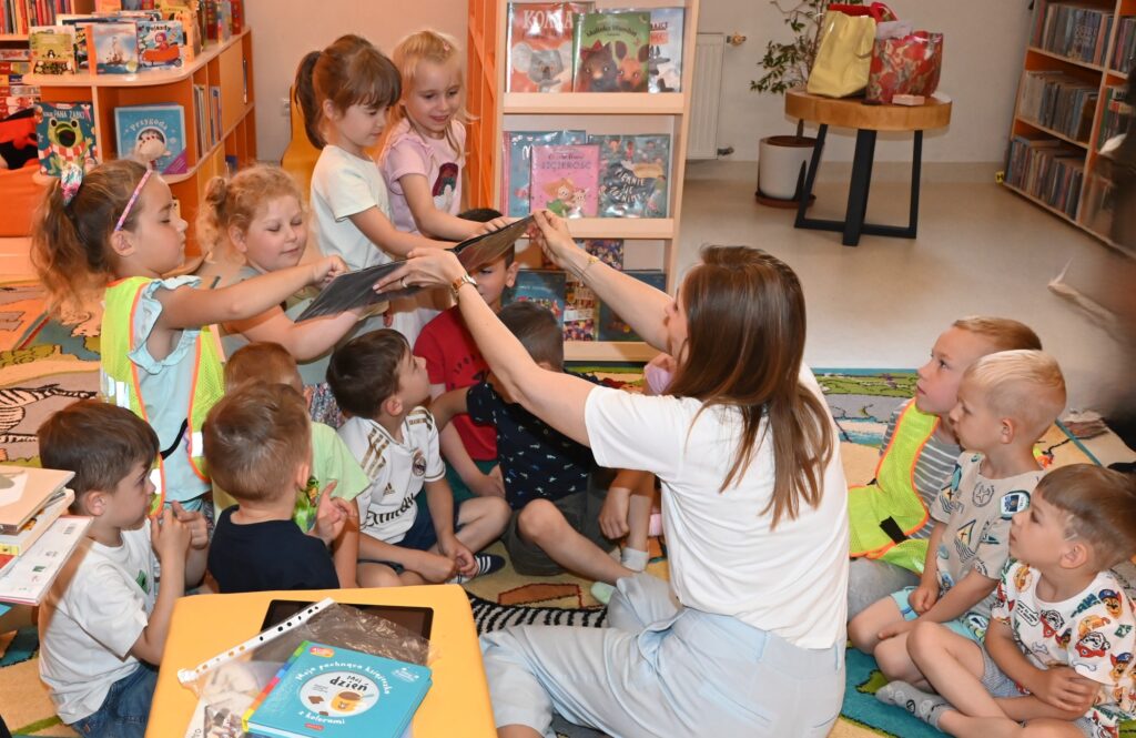 Bibliotekarka Izabela Szczyż pokazuje dzieciom książkę. Dzieci dotykają kartek.