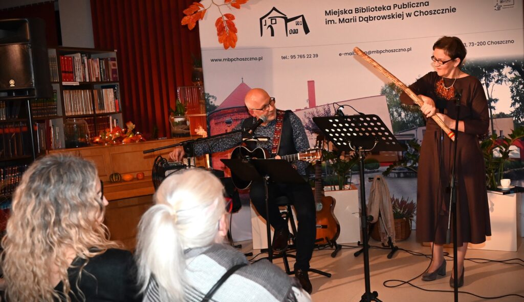 Przed publicznością od lewej: Marek Staniewski, siedzący na krześle i grający na gitarze oraz Marta Staniewska, trzymająca w reku długą "grzechotkę"