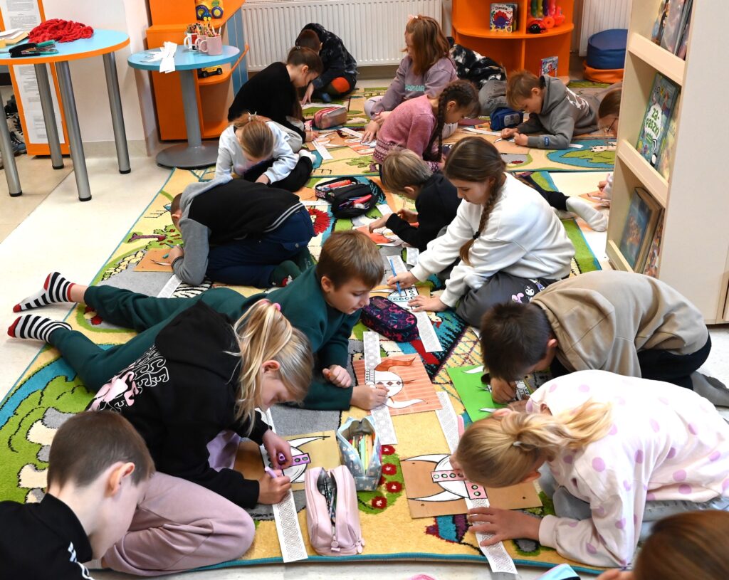 Dzieci na dywanie kolorują hełmy.