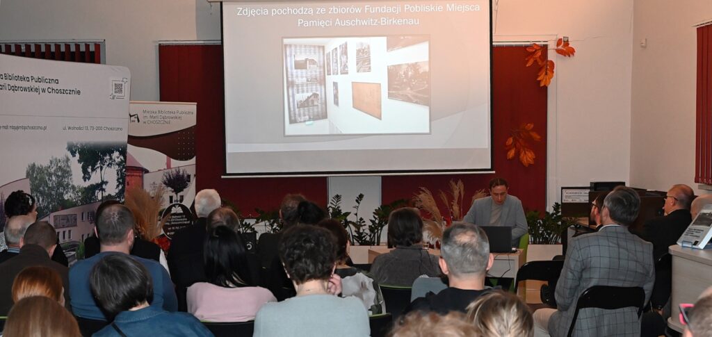 Profesor Wojciech Wichert siedzi w fotelu. Za nim slajd ze zdjęciem IG Farb.