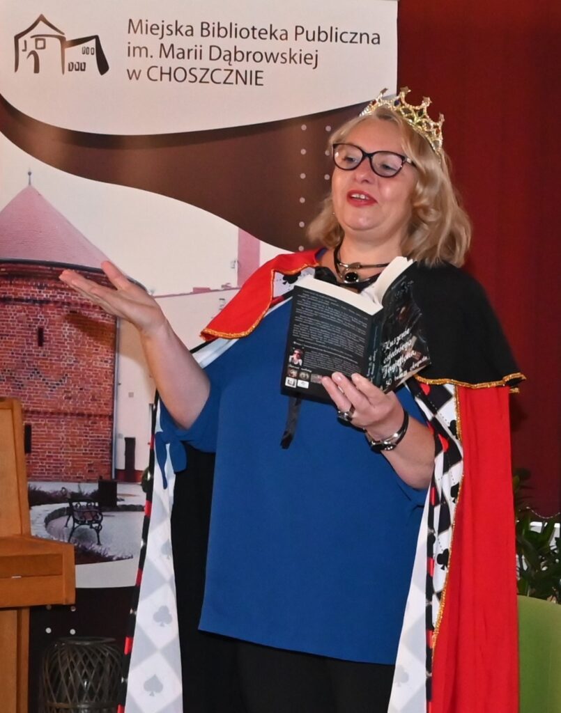 Joanna Kupniewska w koronie i królewskim płaszczu czyta ze swojej książki.
