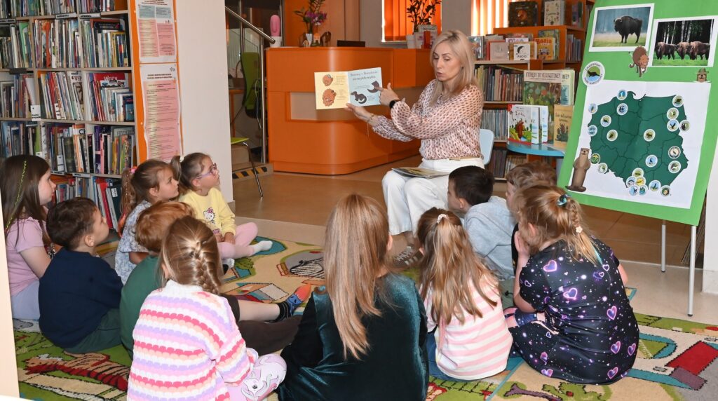 Bibliotekarka Izabela Szczyż pokazuje dzieciom książeczkę.