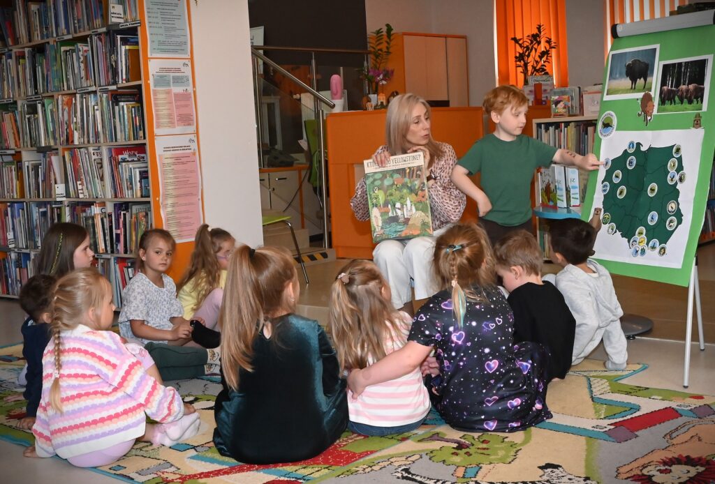 Bibliotekarka Izabela Szczyż trzyma w rękach książkę. Obok niej stoi chłopiec i wskazuje na mapie na Woliński Park NArodowy.
