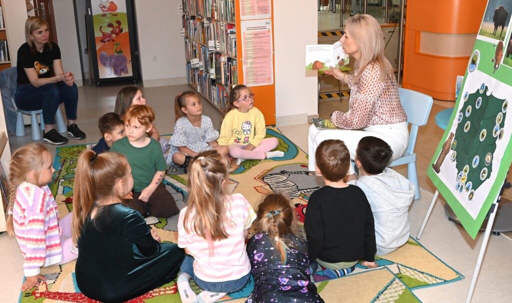 Bibliotekarka Izabela Szczyż czyta dzieciom książeczkę.
