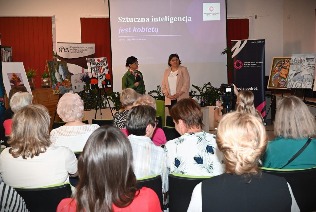 Katarzyna Jezierska i Dorota Dżega-Pietruszkiewicz przed publicznością. Z nimi ekran z wyświetlonym slajdem "Sztuczna inteligencja jest kobietą".