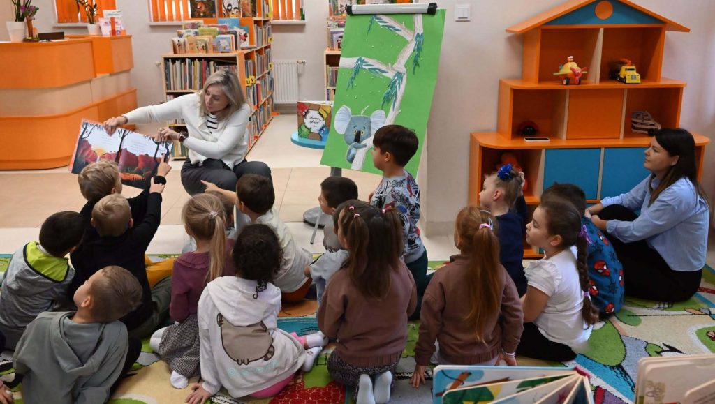 Bibliotekarka Izabela Szczyż pokazuje siedzącym na dywanie dzieciom książkę o koali.