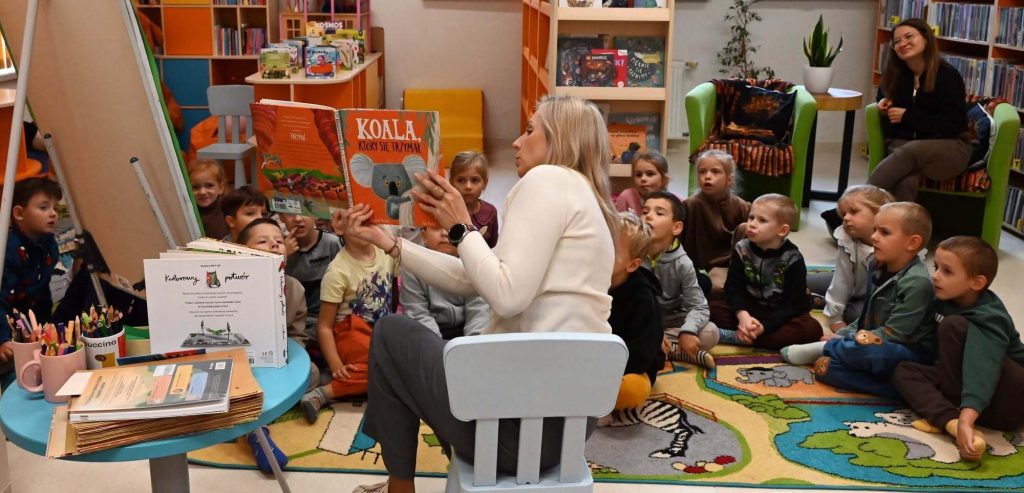Bibliotekarka Izabela Szczyż pokazuje siedzącym na dywanie dzieciom książkę o koali.