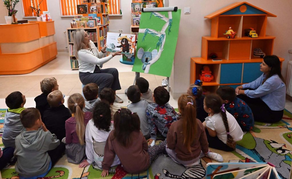 Bibliotekarka Izabela Szczyż pokazuje siedzącym na dywanie dzieciom książkę o koali.