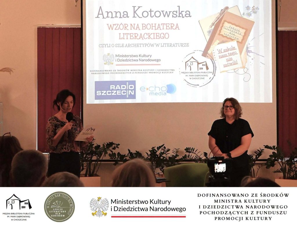 Przed publicznością stoją dyrektor Katarzyna Jezierska i Anna Kotowska. Za nimi na ekranie slajd z tytułem spotkania.